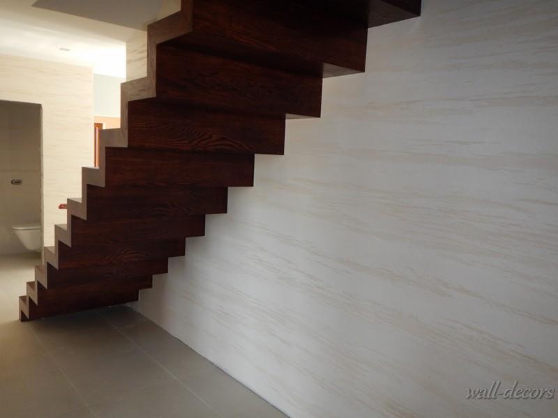 Wnętrze z drewnianymi schodami i ścianą z dekoracyjną fakturą w odcieniach beżu. Widoczny fragment łazienki w tle. Minimalistyczny design.