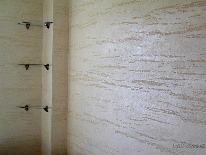 Ściana z dekoracyjną fakturą w odcieniach beżu i bieli. Na ścianie zamontowane trzy szklane półki o zaokrąglonym kształcie, umieszczone pionowo jedna nad drugą.