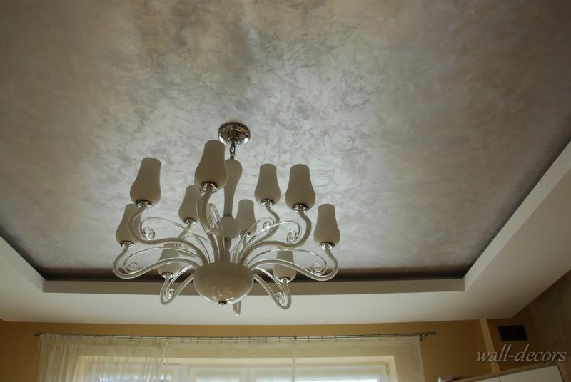 Dekoracyjny sufit w odcieniach szarości z efektem marmuru, oświetlony przez elegancki, biały żyrandol. Widoczna listwa przysufitowa.