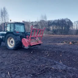 Ciągnik Lamborghini z frezem leśnym na polu po wycince drzew, w tle las i stos pociętych gałęzi.