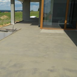 Mix dom wylewki mixokretem Andrzej Jabłoński - Świeżo wylana, gładka posadzka betonowa na tarasie domu w trakcie budowy, widoczny fragment murowanej ściany fundamentowej i krajobraz w tle.