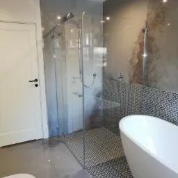 Nowoczesna łazienka z kabiną prysznicową typu walk-in, białą wanną wolnostojącą i szaro-białymi płytkami w geometryczny wzór.