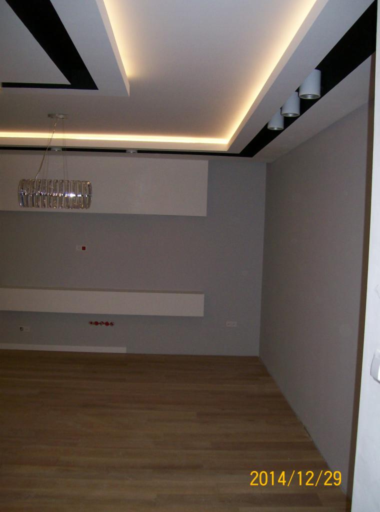 Nowoczesne wnętrze z drewnianą podłogą, szarą ścianą i designerskim oświetleniem sufitowym z elementami czerni i kryształowym żyrandolem. Minimalistyczny wystrój.