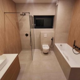 Usługi Remontowo-Budowlane Tip-Top Krzysztof Nidecki - Nowoczesna łazienka z drewnopodobnymi płytkami, czarną armaturą i oknem. Umywalka nablatowa, kabina walk-in i wanna tworzą spójną całość.