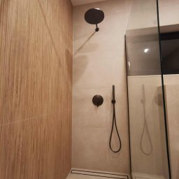 Usługi Remontowo-Budowlane Tip-Top Krzysztof Nidecki - Nowoczesna kabina prysznicowa walk-in z deszczownicą i odpływem liniowym. Ściany wyłożone płytkami imitującymi drewno i jasnymi, beżowymi kaflami. Minimalistyczny design.