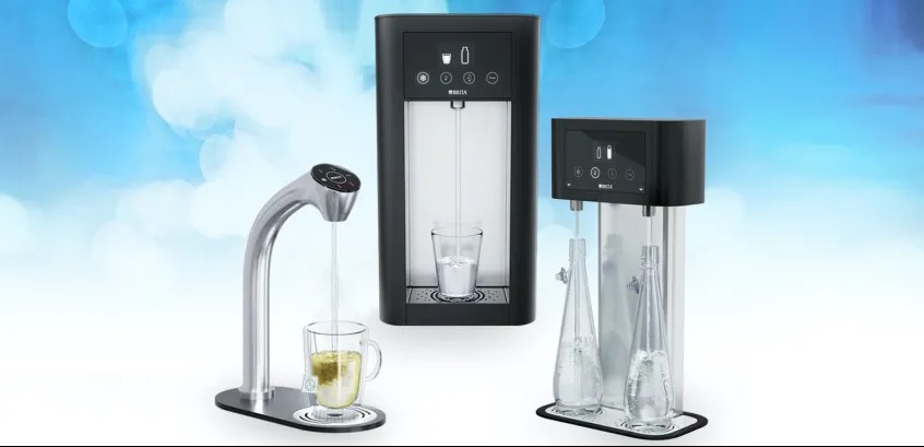 Trzy różne dystrybutory wody, z czego jeden nalewa wodę do szklanki z torebką herbaty, a drugi do szklanki, a trzeci do szklanych butelek wielokrotnego użytku, na rozmytym niebieskim tle.