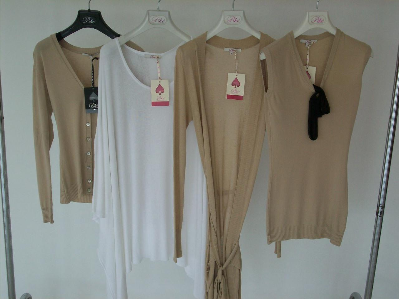 Cztery swetry i bluzki damskie w odcieniach beżu i bieli, wiszące na wieszakach z logo Pike na tle białej ściany.