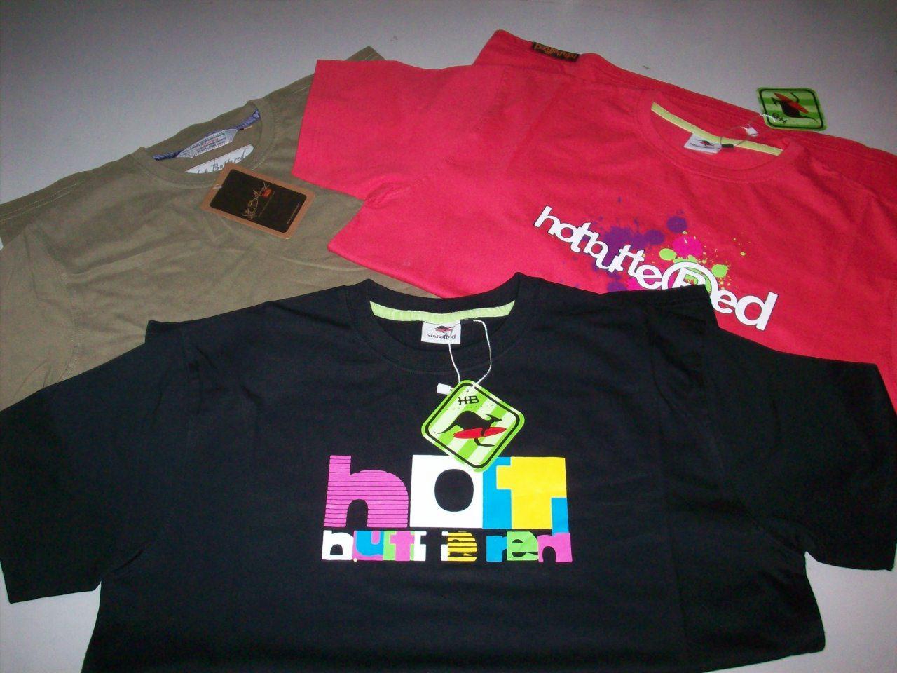 Stos trzech t-shirtów marki Hot Buttered: czarny z kolorowym logo, czerwony z białym napisem i oliwkowy z metką, leżące na szarym tle.