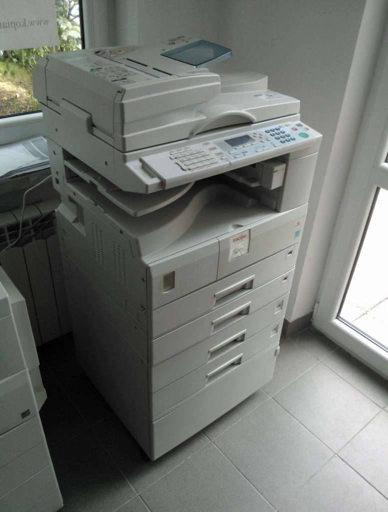Kserokopiarka Ricoh Aficio MP 2000 w jasnym pomieszczeniu z szarymi płytkami podłogowymi, widoczne cztery szuflady na papier.