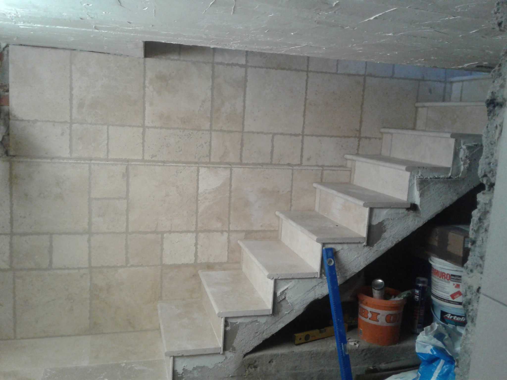 Wykończone płytkami schody w Istebnej. Widoczne narzędzia glazurnicze i wiaderka z zaprawą. Ściany również wyłożone płytkami w jasnym odcieniu.