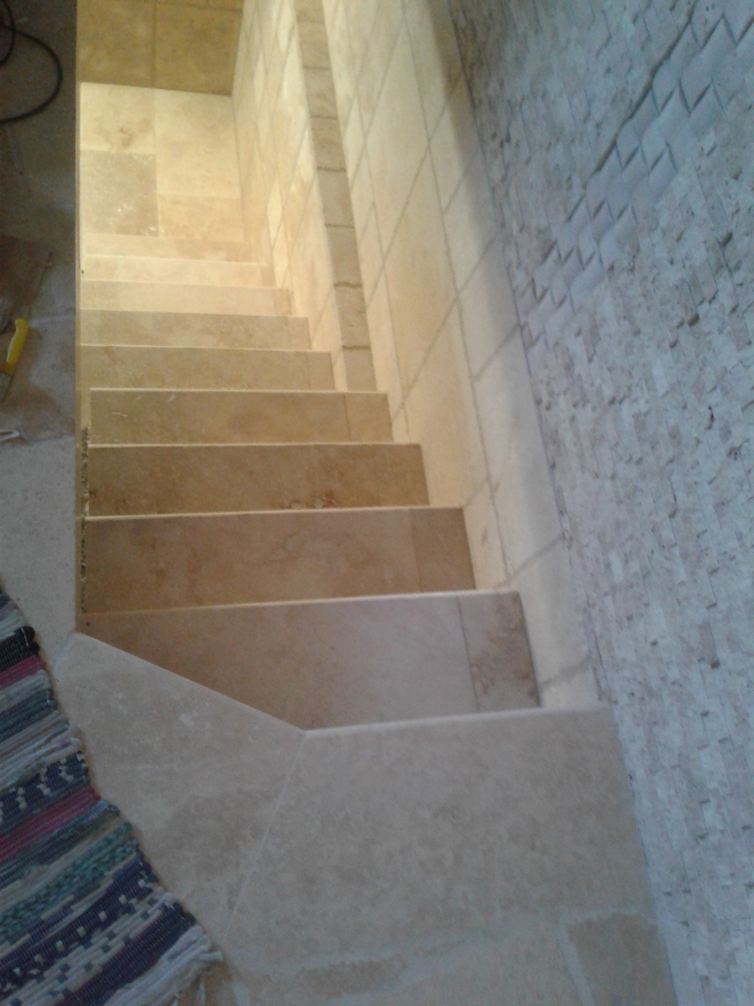 Wykończone schody z płytek w odcieniach beżu, z widoczną mozaiką na ścianie i fragmentem dywanika. Ujęcie z góry, podkreślające detale wykończenia.