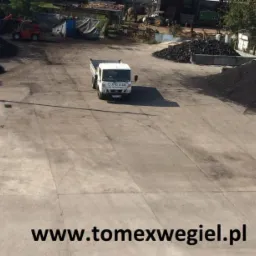 Widok z góry na plac składowy z hałdami węgla, wagą najazdową i samochodem dostawczym na tle magazynu, na dole widoczny adres strony internetowej.