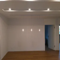 Jasne, świeżo pomalowane wnętrze z parkietem, trzema wiszącymi lampami i oświetleniem sufitowym.