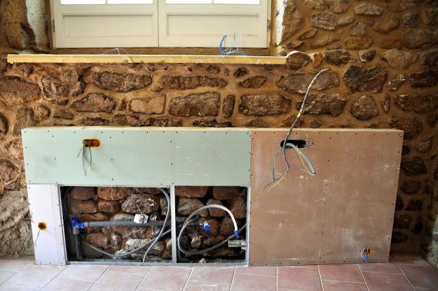 Surowy montaż ścianki działowej z płyt kartonowo-gipsowych w Rawiczu, z widocznymi instalacjami wodnymi i elektrycznymi w przestrzeni pod oknem na tle kamiennej ściany.