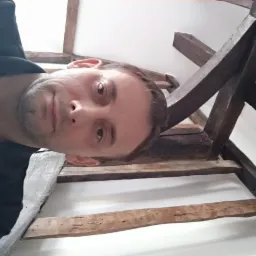 Mężczyzna z bliska, spoglądający w dół, z widoczną drewnianą konstrukcją stropu. Nietypowy kadr z dołu. Ujęcie od dołu na drewniane belki.