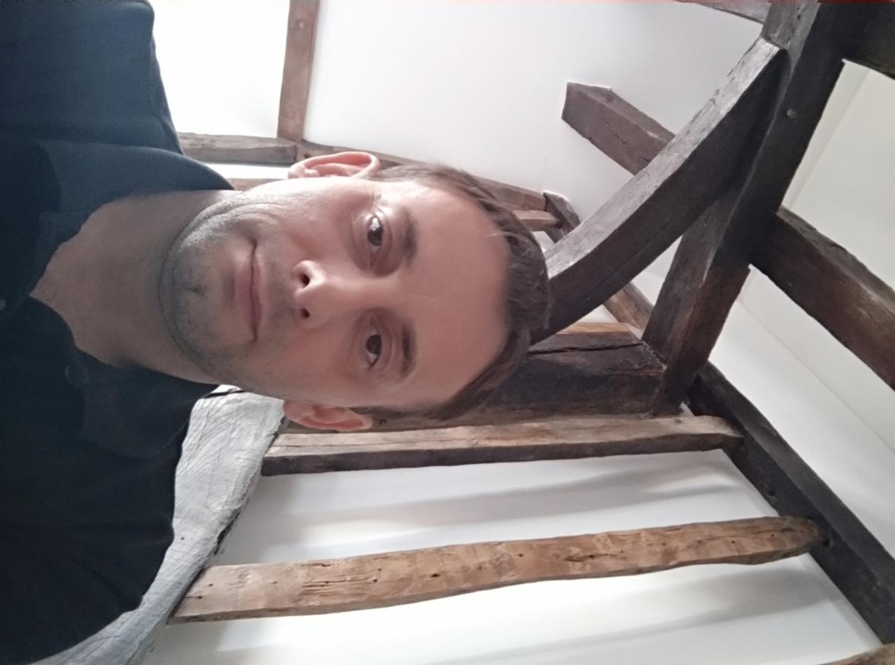 Mężczyzna z bliska, spoglądający w dół, z widoczną drewnianą konstrukcją stropu. Nietypowy kadr z dołu. Ujęcie od dołu na drewniane belki.