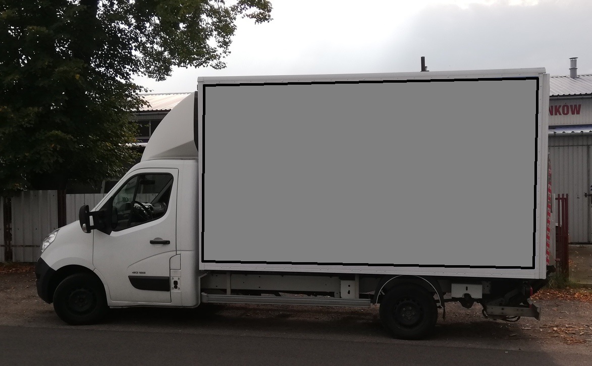 Biały samochód dostawczy z pustą przestrzenią ładunkową, zaparkowany na ulicy z widocznym budynkiem w tle.