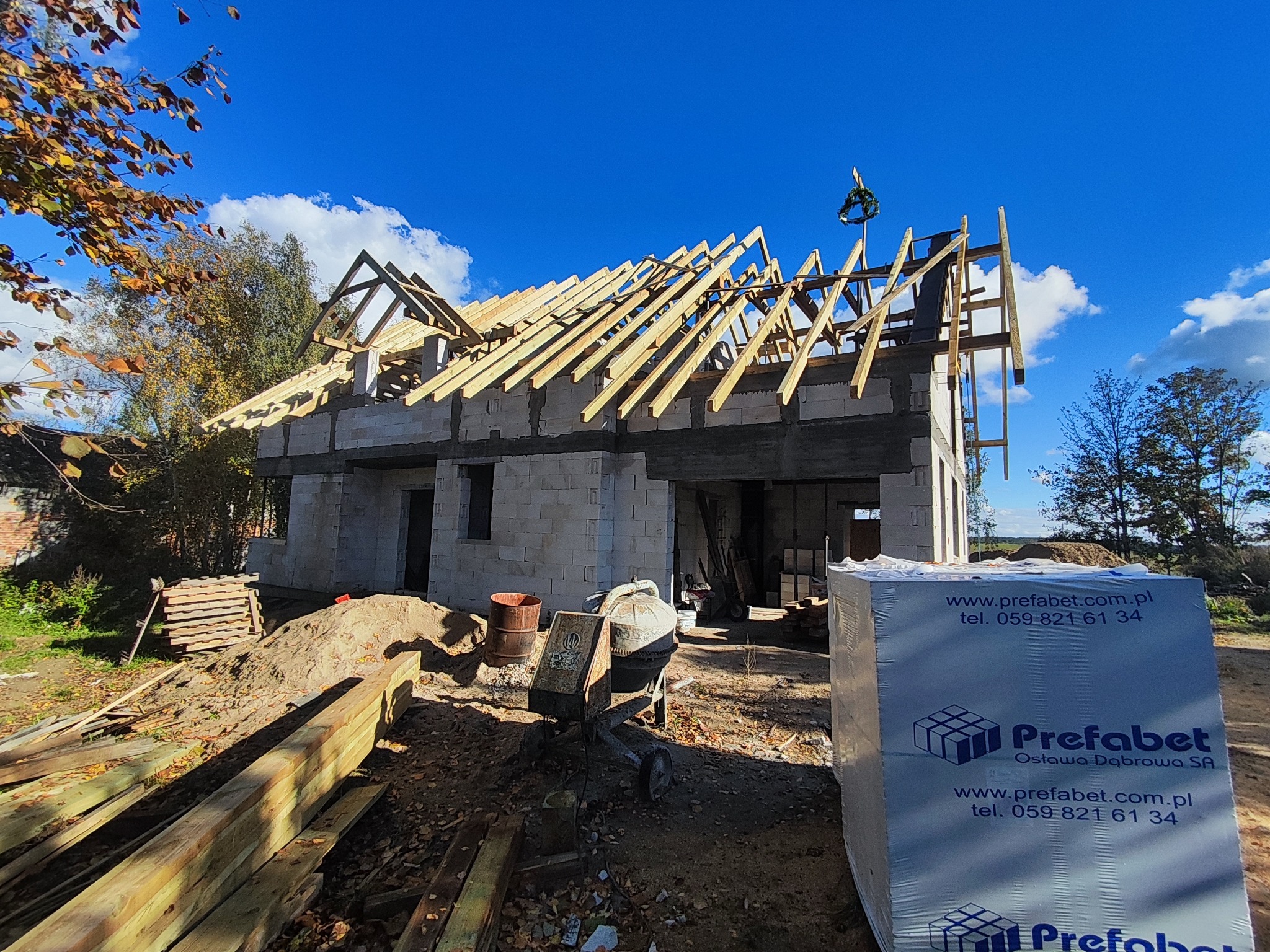 Budowa domu z białych bloczków: wznoszenie drewnianej konstrukcji dachu. Na pierwszym planie materiały budowlane marki Prefabet.