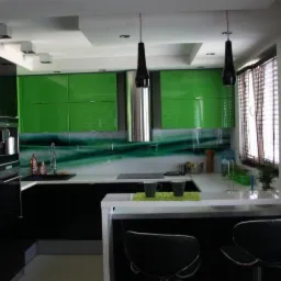 Nowoczesna kuchnia z czarno-zielonymi szafkami na wysoki połysk, białym blatem i wyspą z dwoma czarnymi krzesłami barowymi.