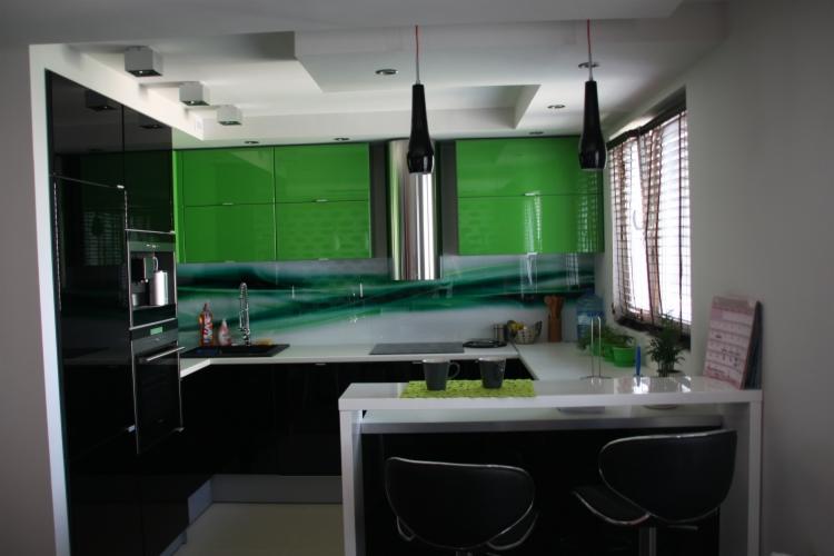 Nowoczesna kuchnia z czarno-zielonymi szafkami na wysoki połysk, białym blatem i wyspą z dwoma czarnymi krzesłami barowymi.
