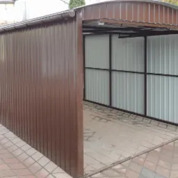 Otwarta, brązowa brama garażowa z blachy trapezowej, widok z boku na podjeździe z kostki brukowej, z widocznym mechanizmem sprężynowym.