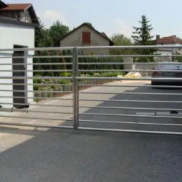 Nowoczesna, pozioma brama wjazdowa ze stali nierdzewnej, z automatycznym napędem, na tle domu i podjazdu.