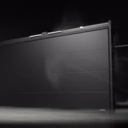 Ciemnoszara, segmentowa brama garażowa z widocznym mechanizmem sprężynowym i subtelnym oświetleniem podłogowym tworzącym efekt mgły.