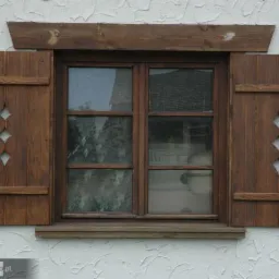 Drewniane okno z otwartymi okiennicami z wyciętymi rombami na tle białej, chropowatej ściany. Widoczny drewniany nadproże i parapet.