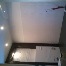 Wykończona łazienka z białymi płytkami 3D na ścianach, czarną podłogą i sufitem z oświetleniem punktowym. Widok z dołu, podkreślający geometrię i nowoczesny design.