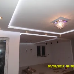 Nowoczesny sufit podwieszany z oświetleniem LED i kryształowym żyrandolem w przestronnym wnętrzu w trakcie wykańczania.