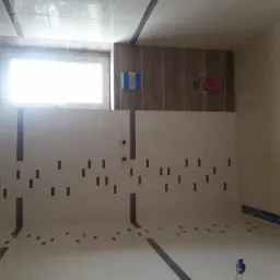 Łazienka w trakcie remontu: ułożone płytki ścienne z dekoracyjnymi brązowymi wstawkami, widoczne przygotowane punkty instalacji wodnej, częściowo ułożona podłoga z ciemniejszymi płytkami.