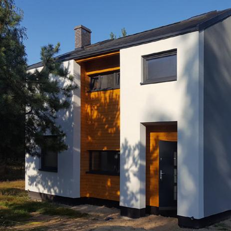 Nowoczesny dom z elewacją w kolorze białym i drewnianą okładziną, ciemne okna, widok z zewnątrz w słoneczny dzień.