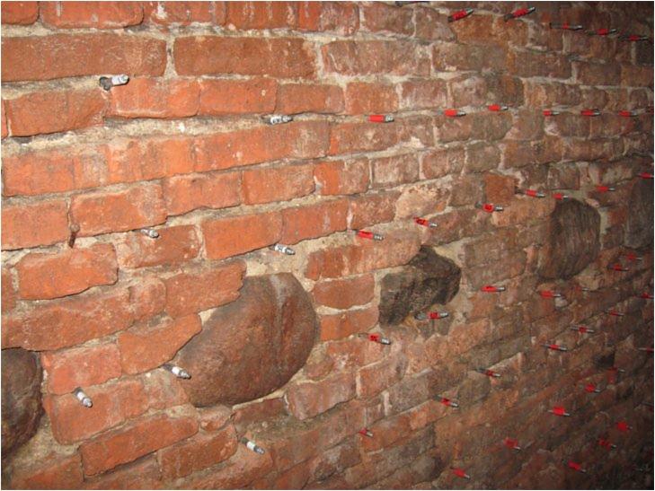 Ceglana ściana z widocznymi iniektorami żywicy poliuretanowej WEBAC 1404, aplikowanymi w celu wzmocnienia struktury i uszczelnienia przed wilgocią.