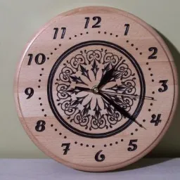 Okrągły zegar ścienny z jasnego drewna z czarnymi cyframi i ornamentem w centrum tarczy, wskazujący godzinę około 10:22.