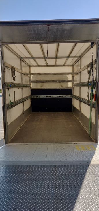 Pusta przestrzeń ładunkowa busa z otwartą rampą załadunkową, widoczne zabezpieczenia ładunku na ścianach i suficie.