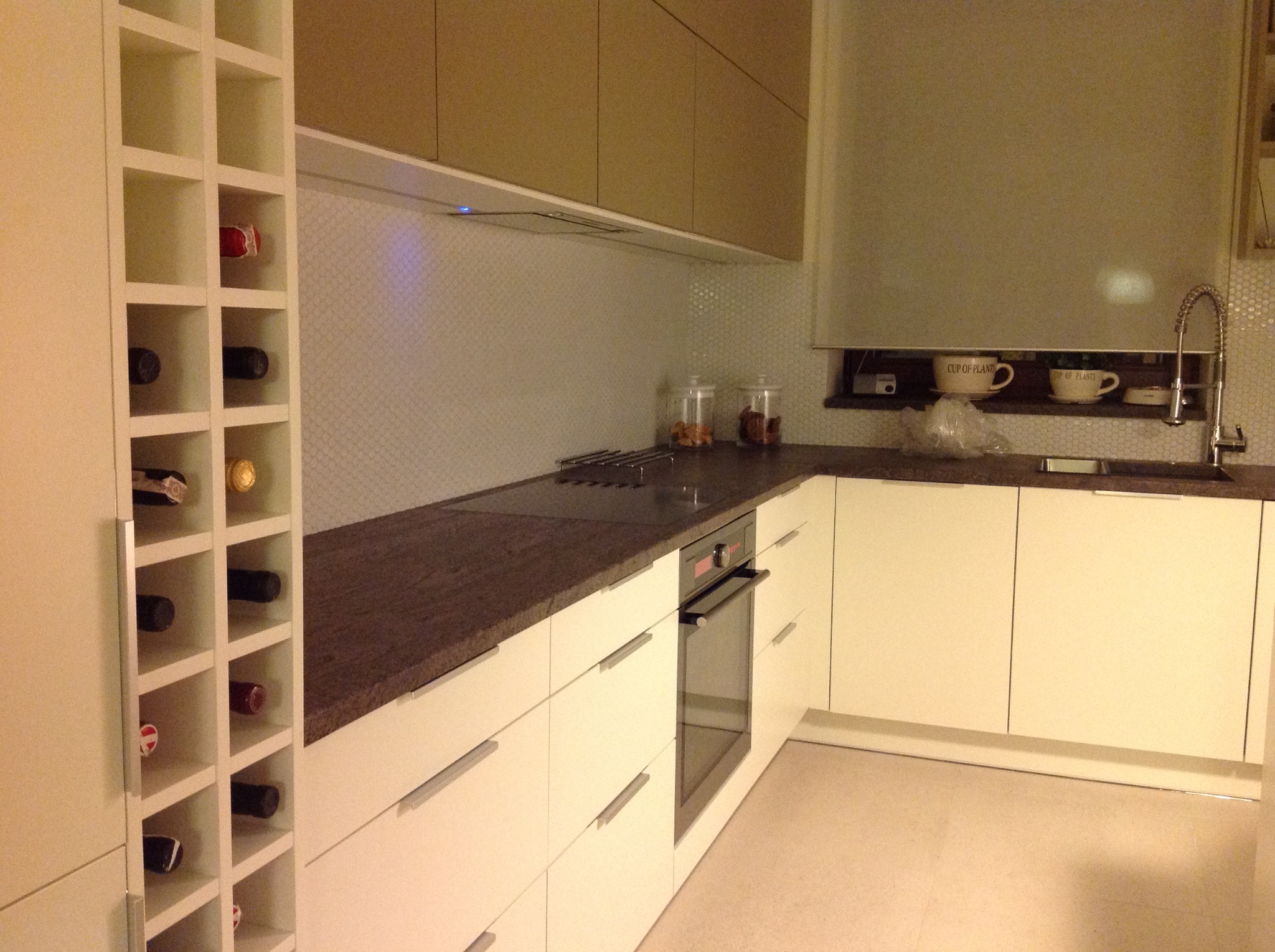 Nowoczesna kuchnia z białymi szafkami, brązowym blatem, płytą indukcyjną, piekarnikiem i regałem na wino, widok z perspektywy.