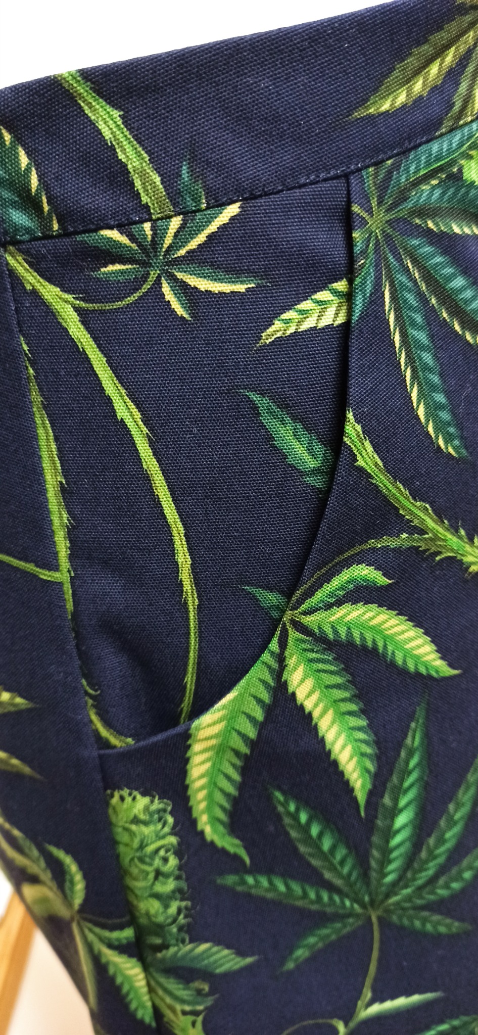 Fragment uszytych spodni z kieszenią, wykonanych z granatowego materiału w zielone liście konopi.