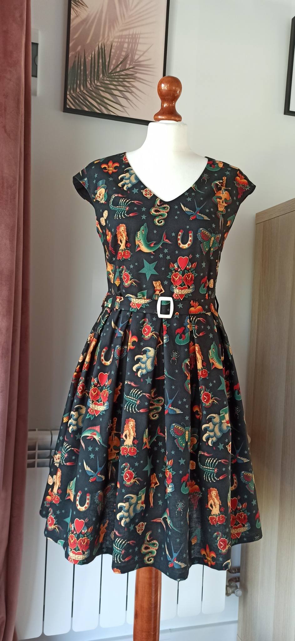 Czarna sukienka z krótkim rękawem, w stylu retro, z nadrukiem tatuaży old school, zaprezentowana na manekinie z drewnianą podstawą.