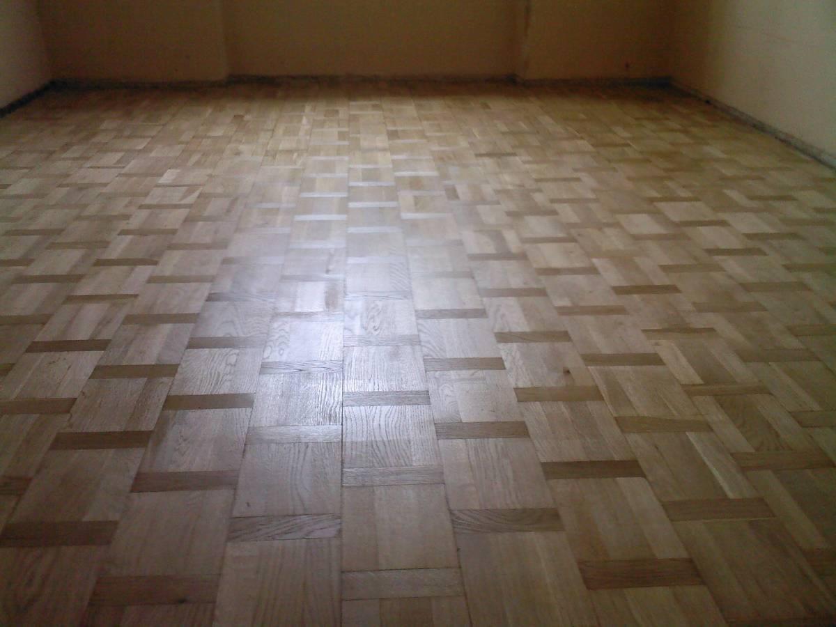 Wzór parkietu ułożonego z jasnego drewna w jodełkę francuską, widoczne ślady po renowacji.