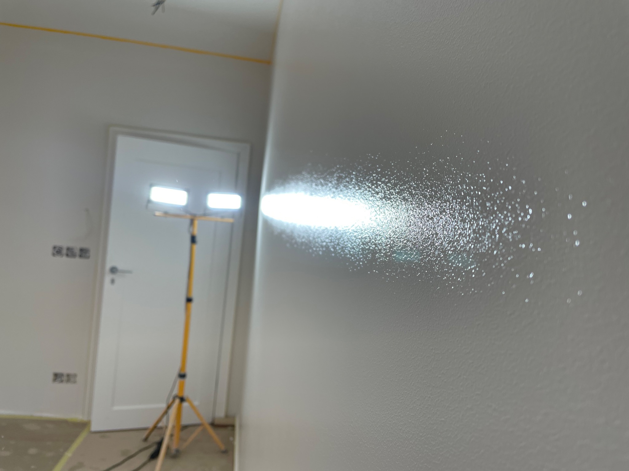 Świeżo pomalowana ściana w pokoju, oświetlona lampą roboczą, uwidaczniająca fakturę i niedoskonałości powierzchni.