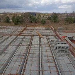 Wieniec stropowy Teriva zbrojony stalą, widok z góry na budowę domu jednorodzinnego, w tle zalesiony teren i pochmurne niebo.