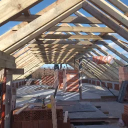 Konstrukcja drewniana dachu w trakcie budowy domu murowanego, widoczne krokwie, murłat i pustaki ceramiczne Termoton