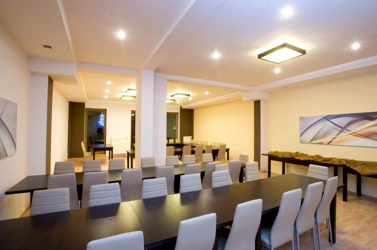 Sala konferencyjna z długimi, ciemnymi stołami i jasnymi krzesłami w Bydgoszczy, oświetlona nowoczesnymi lampami sufitowymi, z abstrakcyjnym obrazem na ścianie.