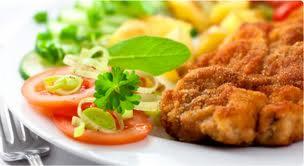 Apetycznie wyglądający kotlet schabowy w panierce, podany z ziemniakami, sałatką ze świeżych ogórków i pomidorów, udekorowany zieloną pietruszką i porem.