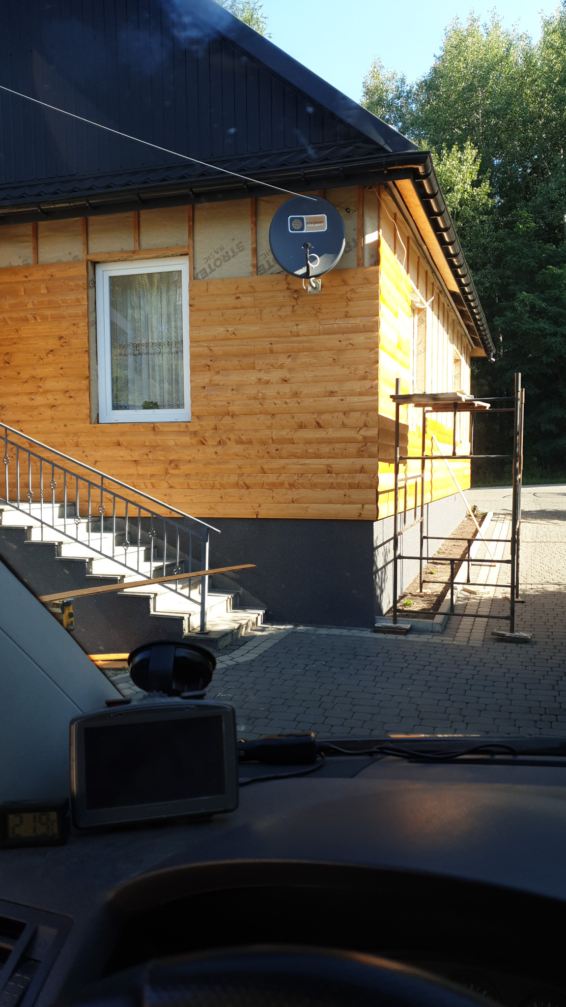 Dom w trakcie prac elewacyjnych: drewniana boazeria, ocieplenie, rusztowanie, schody z metalową barierką i satelita na ścianie, widok z wnętrza pojazdu.