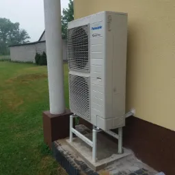 Zewnętrzna jednostka klimatyzacji Panasonic Inverter zamontowana na metalowym stelażu przy budynku w Siedlcach, widoczne elementy instalacji elektrycznej i fragment fundamentu.