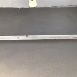 Świeżo wylana, szara posadzka wyrównywana długą, aluminiową łatą; widoczny fragment ściany z niedokończonym tynkiem.