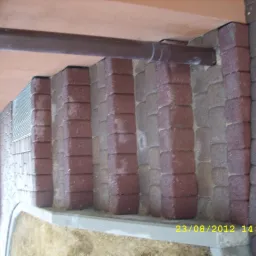 Schody z kostki brukowej w odcieniach brązu i szarości, z widocznym orynnowaniem i fragmentem elewacji. Ujęcie z bliska, podkreślające detale wykończenia.