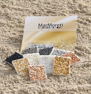 Prezentacja próbek dekoracyjnych kamieni w kwadratowych formach na tle piaszczystej powierzchni, z widocznym katalogiem marki Marmoreti Natural Colors.