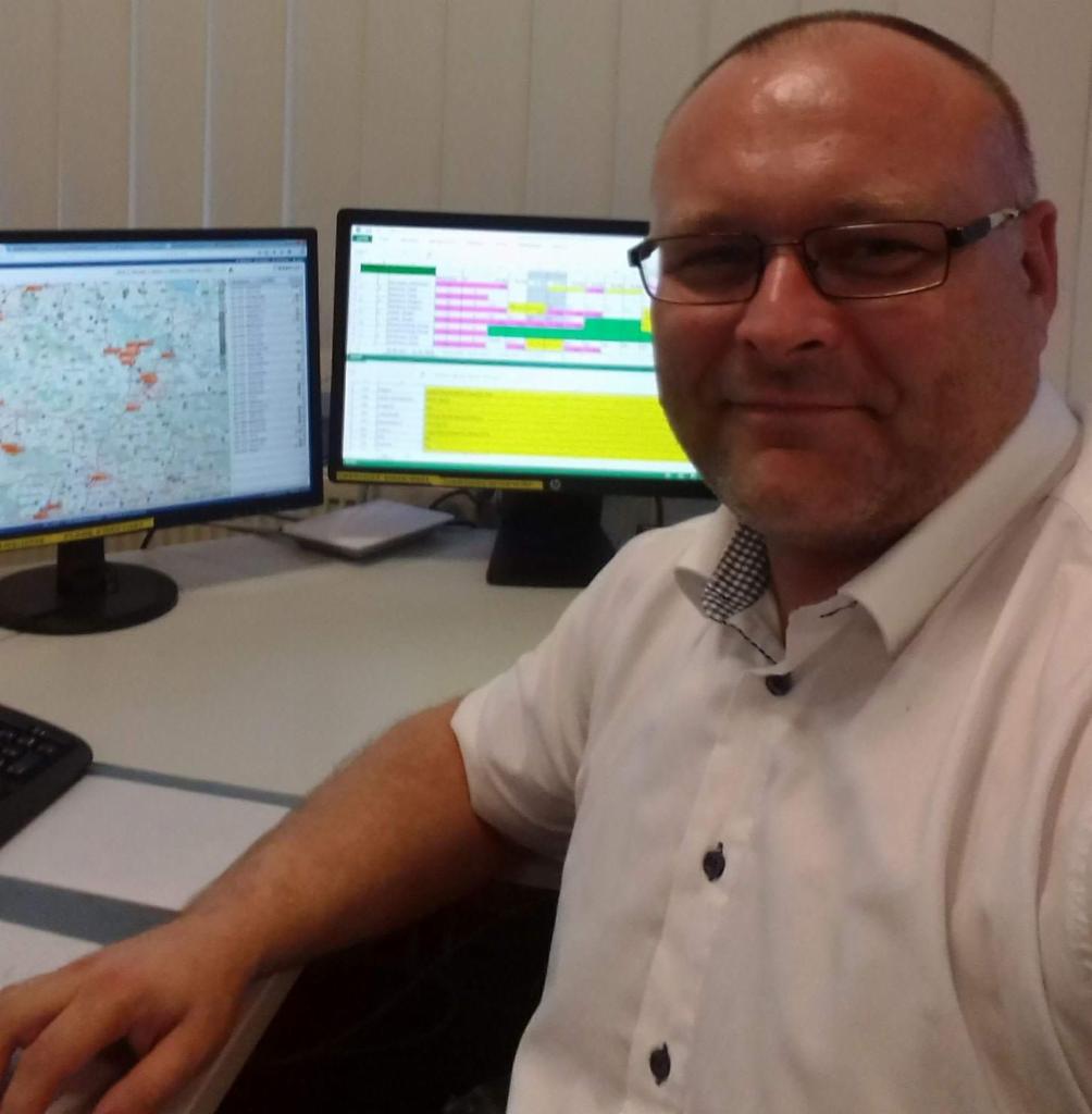 Dyspozytor w okularach przed dwoma monitorami, jeden z mapą, drugi z harmonogramem transportu.